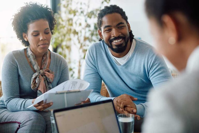 A couple reviews a life insurance denial letter and medical records at a kitchen table.